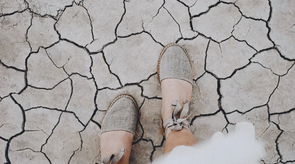 Person's feet in canvas shoes standing on dry cracked ground surface