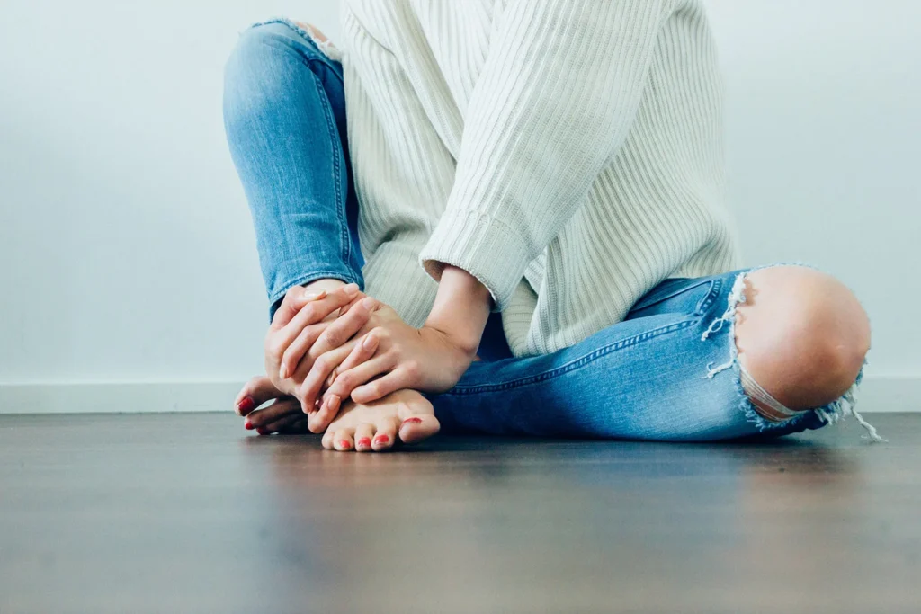 Person sitting on floor holding bare feet with both hands