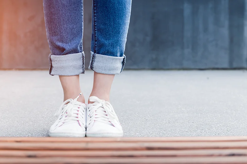 Person standing outdoors wearing white sneakers and rolled denim jeans showing ankles