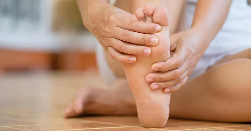 Person sitting on floor holding and massaging the arch of their foot