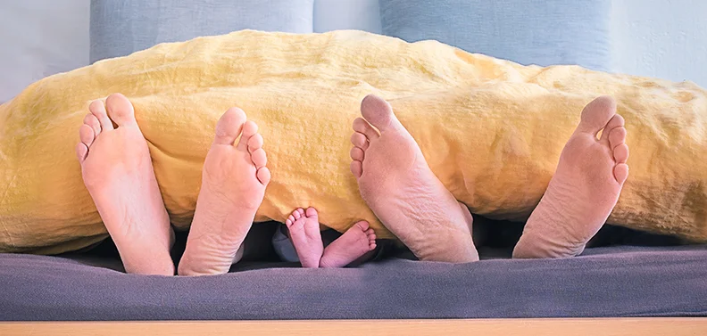 Adult and infant bare feet visible at the edge of a bed