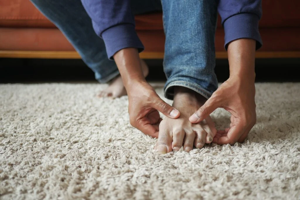 Person experiencing foot pain and massaging their foot at home